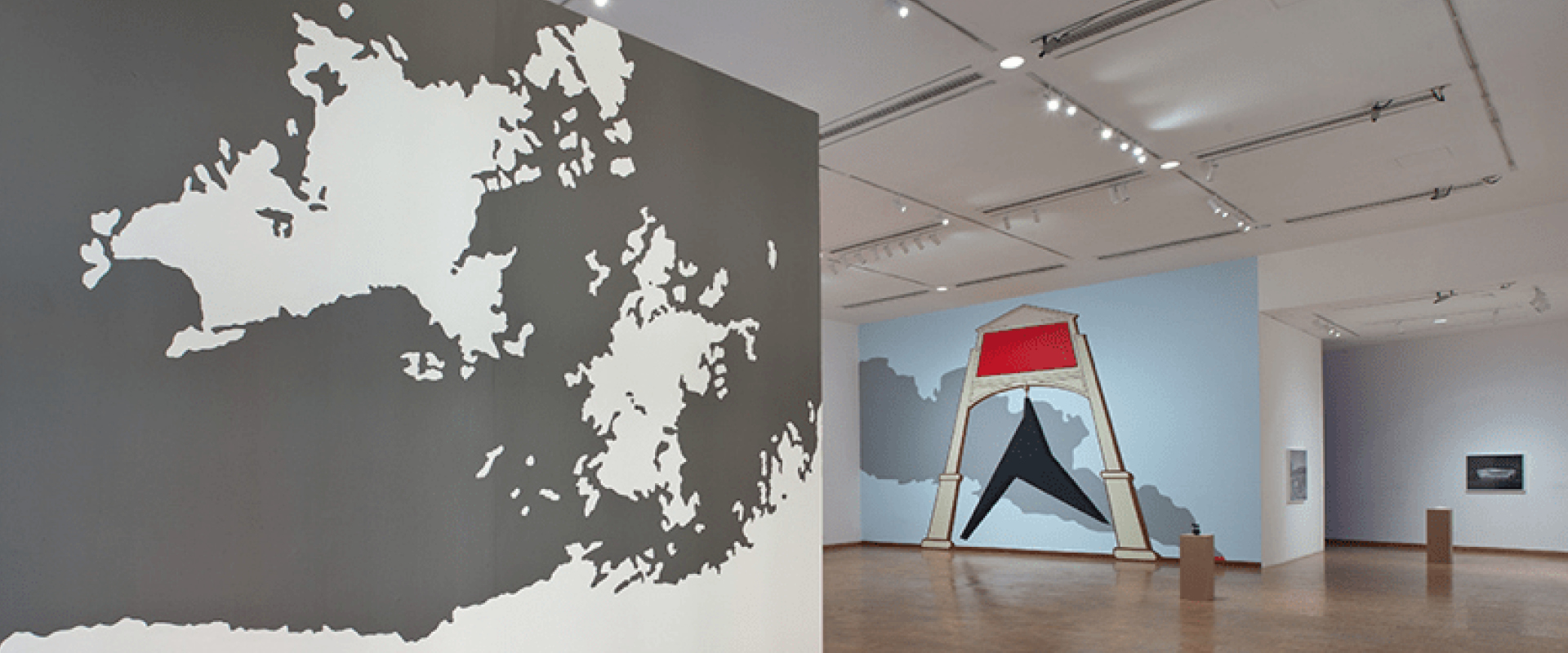 Art gallery interior with large abstract wall murals, including a black and white geographic shape on the left and a bold geometric design with red and blue in the background.