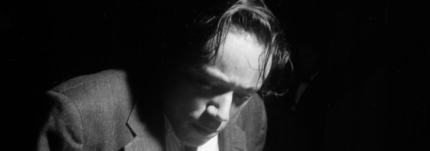 A monochromxe image capturing a moment of deep concentration, where a man is engrossed in reading or examining something out of frame, lit dramatically from the side to create a play of light and shadow.