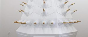 Large white geometric structure with multiple protruding gold and white cone-shaped objects arranged in a pattern on its surface.