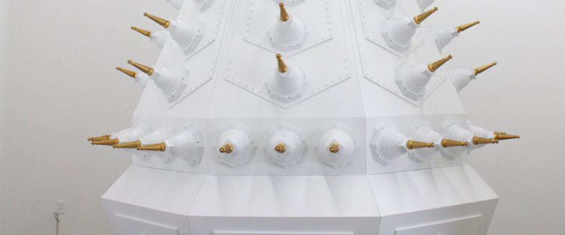 Large white geometric structure with multiple protruding gold and white cone-shaped objects arranged in a pattern on its surface.