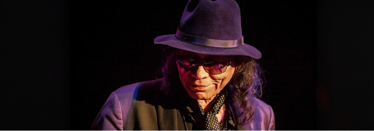 A somber figure, Rodriguez, in a stylish hat casts a mysterious shadow