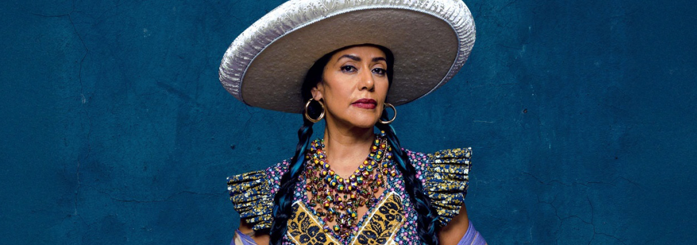 Lila Downs poses with a sombrero behind a dark blue background