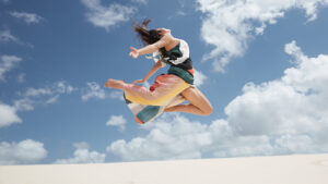 A woman mid-leap against a backdrop of a clear sky, her colorful skirt flowing with the motion.