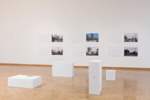 Modern art gallery with photographs exhibited on a white wall above minimalist white plinths.