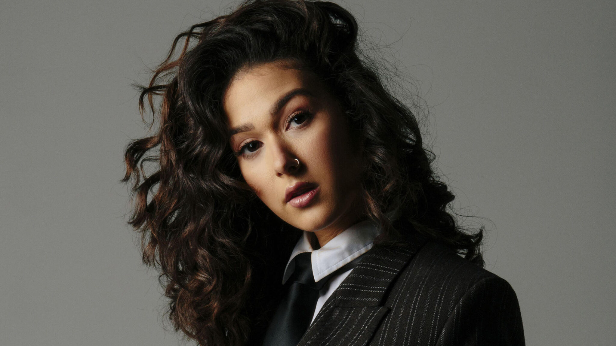Confident woman with curly hair and a serious look, wearing a business suit with a modern twist.