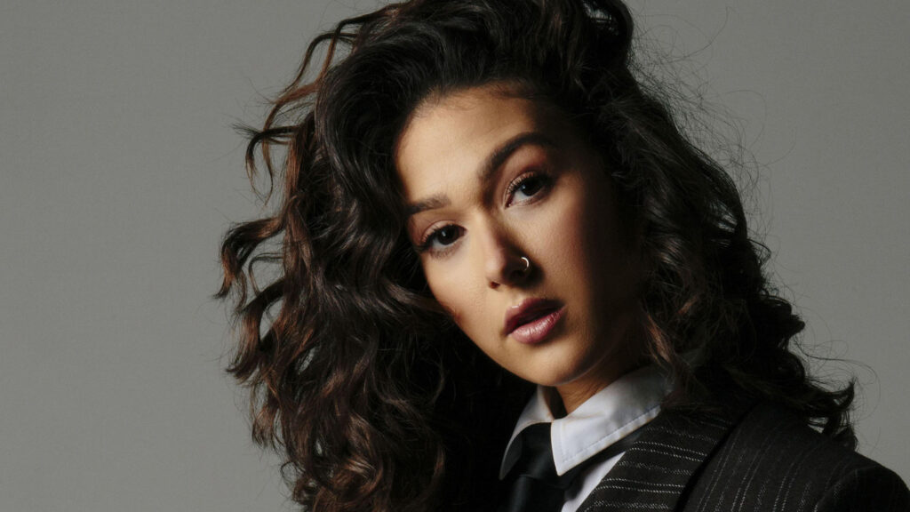 Confident woman with curly hair and a serious look, wearing a business suit with a modern twist.