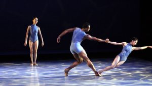 Three contemporary dancers on stage performing a fluid and expressive routine with dynamic poses under a soft spotlight.