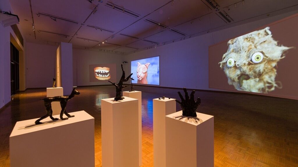 An eclectic modern art gallery showcasing sculptures and whimsical animal-themed projections.