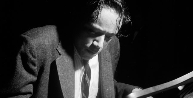 A monochrome image capturing a moment of deep concentration, where a man is engrossed in reading or examining something out of frame, lit dramatically from the side to create a play of light and shadow.