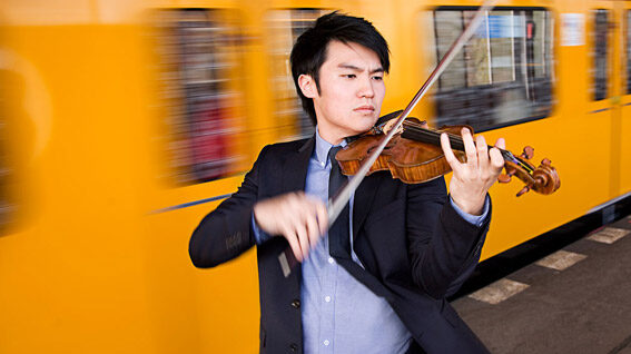 A focused violinist plays his instrument with passion against the backdrop of a swiftly moving yellow train.