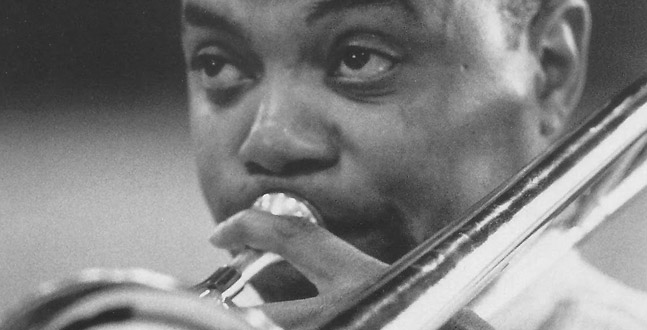 A close-up black and white photo of a jazz musician passionately playing the trumpet.