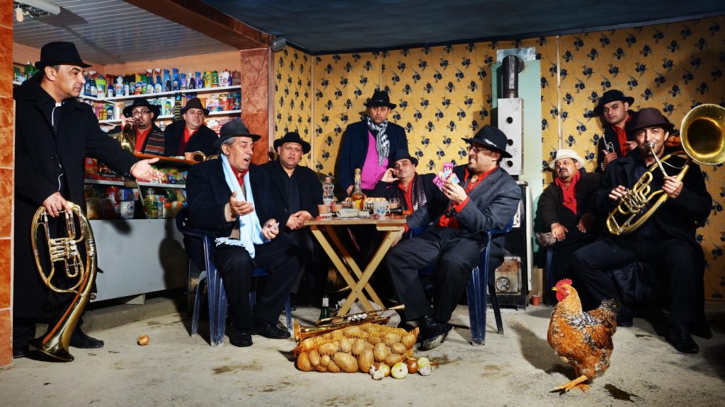 A lively scene in a rustic room with a group of musicians and individuals engaged in animated conversation, with instruments, a chicken and onions scattered on the floor, creating an atmosphere of an impromptu gathering or celebration.