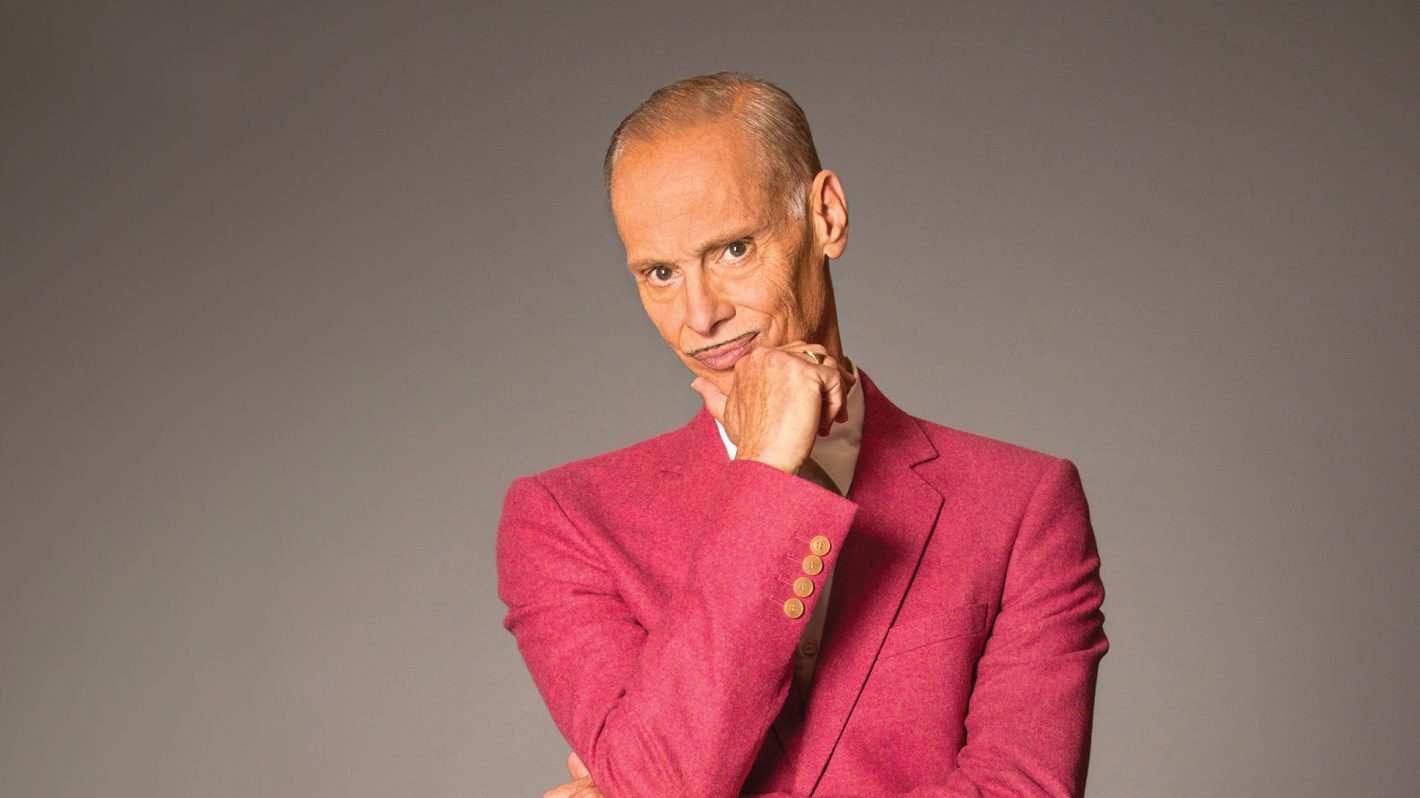 A confident individual in a striking pink suit, striking a thoughtful pose with a hand on their chin.