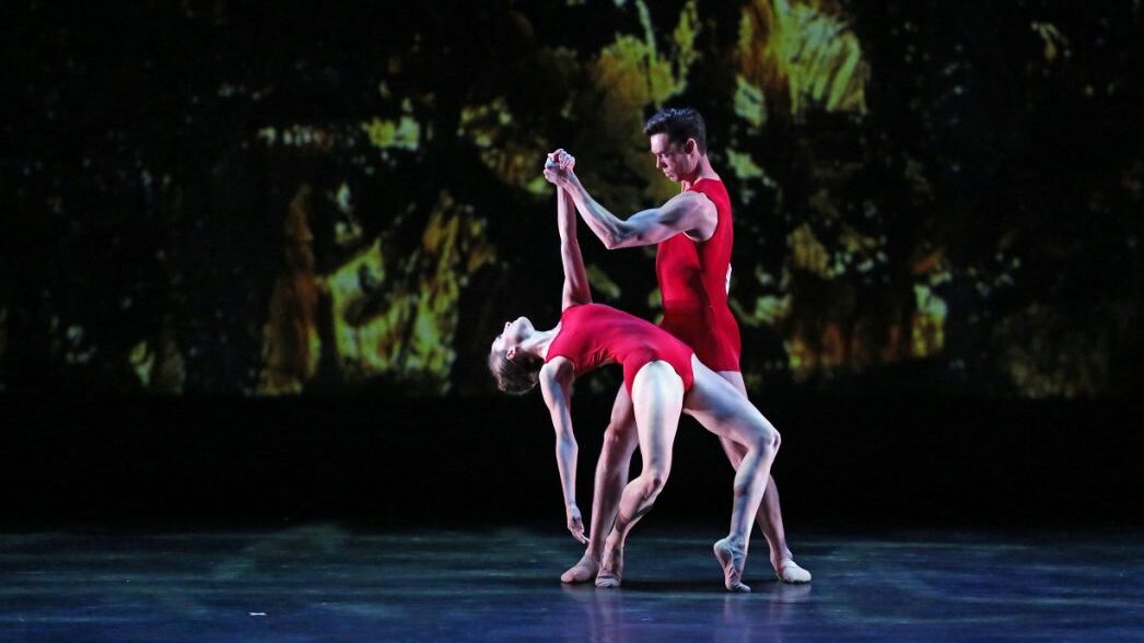 Two dancers in a graceful pose on stage, exhibiting the beauty of contemporary dance against a projected backdrop.