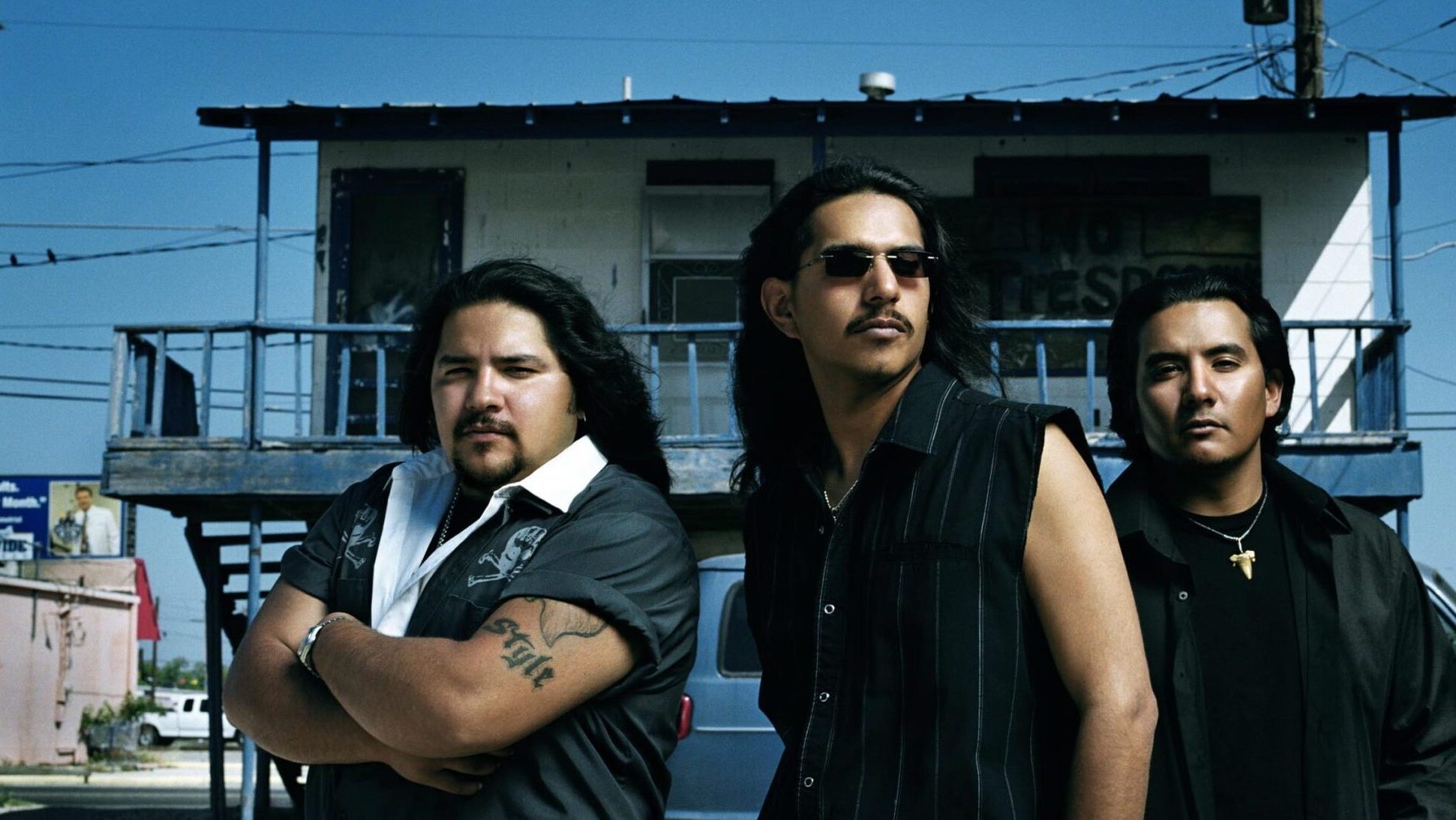 Three men standing confidently in front of a building with a gritty backdrop, exuding a cool and rugged charisma.