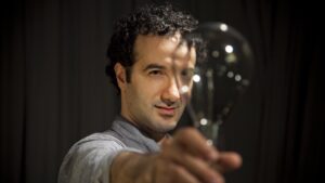 A man holding a light bulb in focus, symbolizing an idea or inspiration, with a look of contemplation on his face.