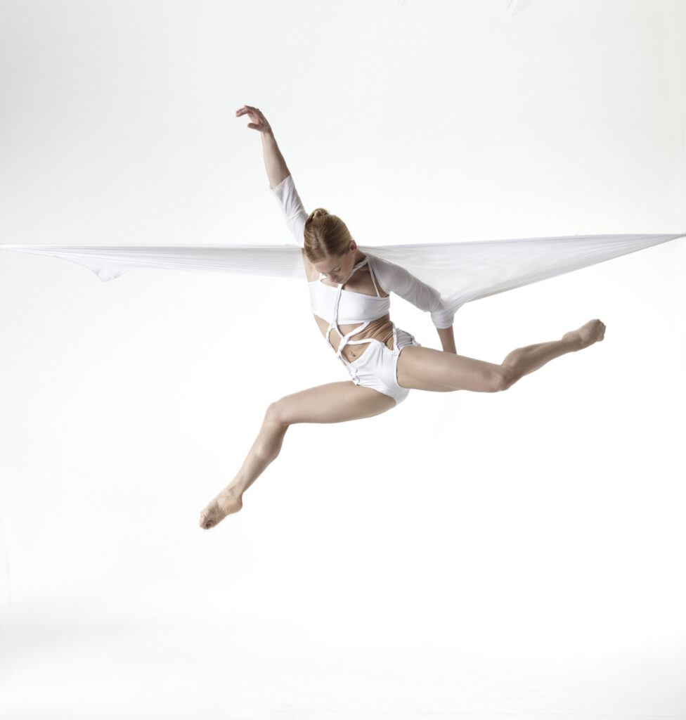 Graceful dancer leaping through the air with a flowing white fabric accentuating her movement.