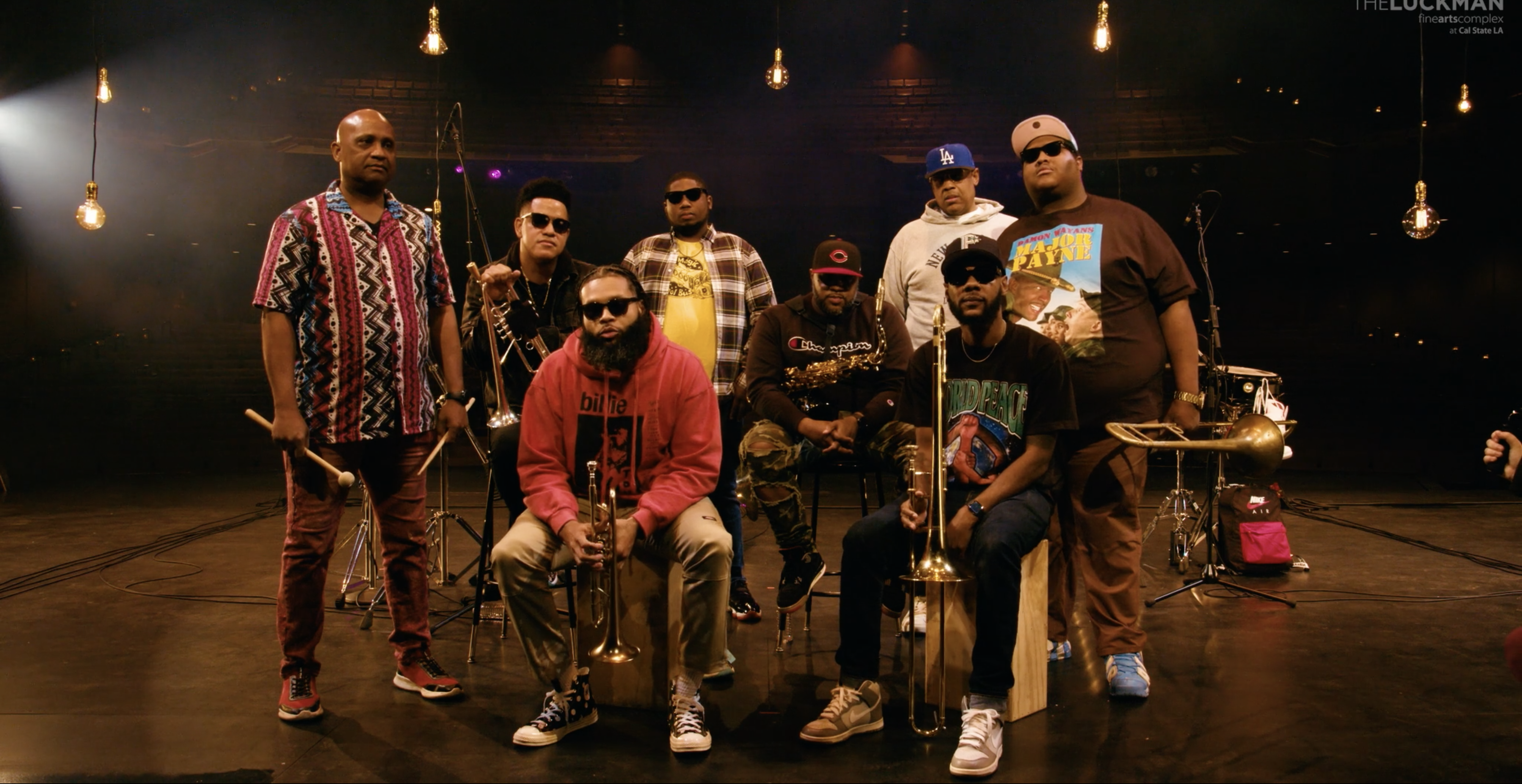 The Soul Rebels posing on a theater stage with hanging lights in background.