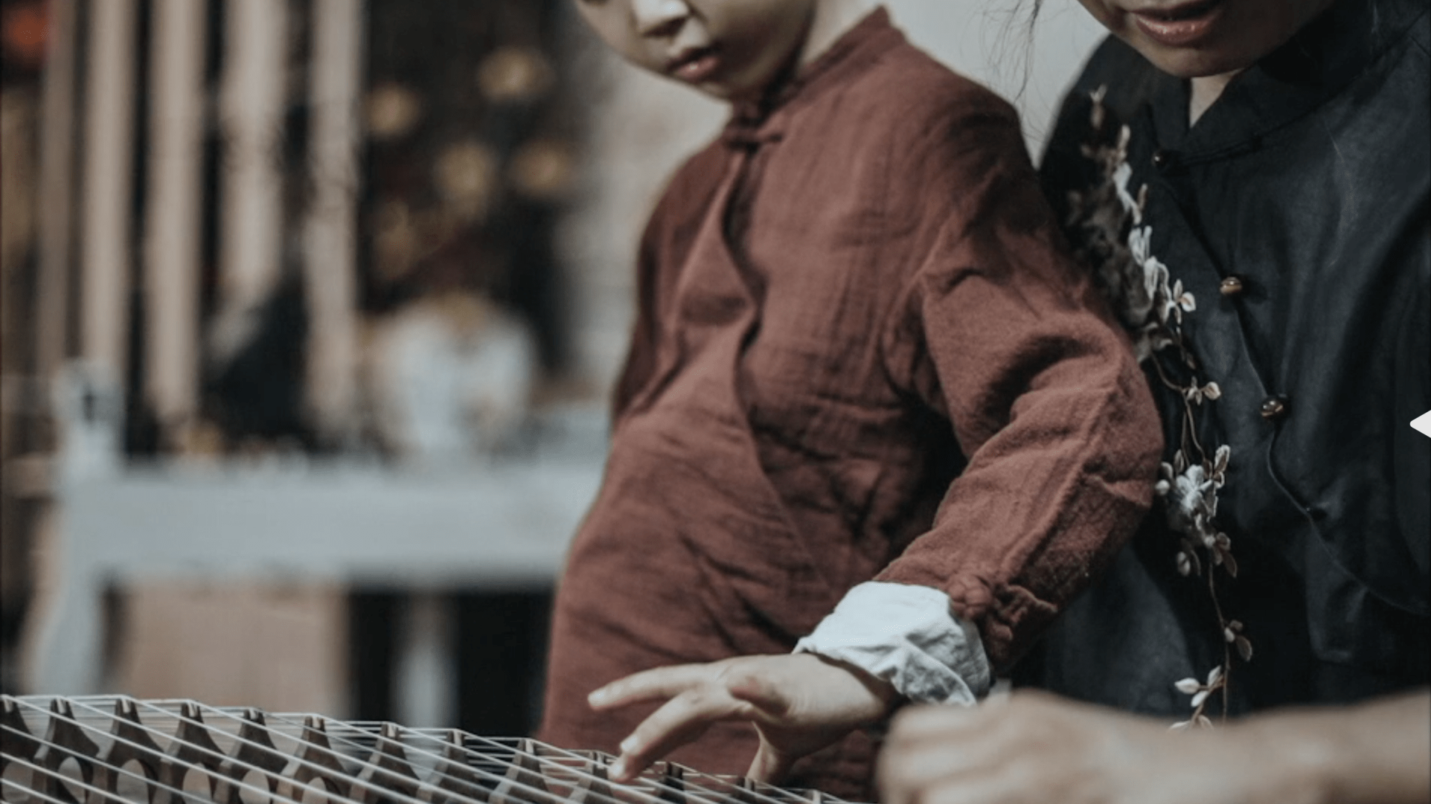 Two people collaboratively working on a traditional weaving loom, with a focus on their hands guiding the fabric.