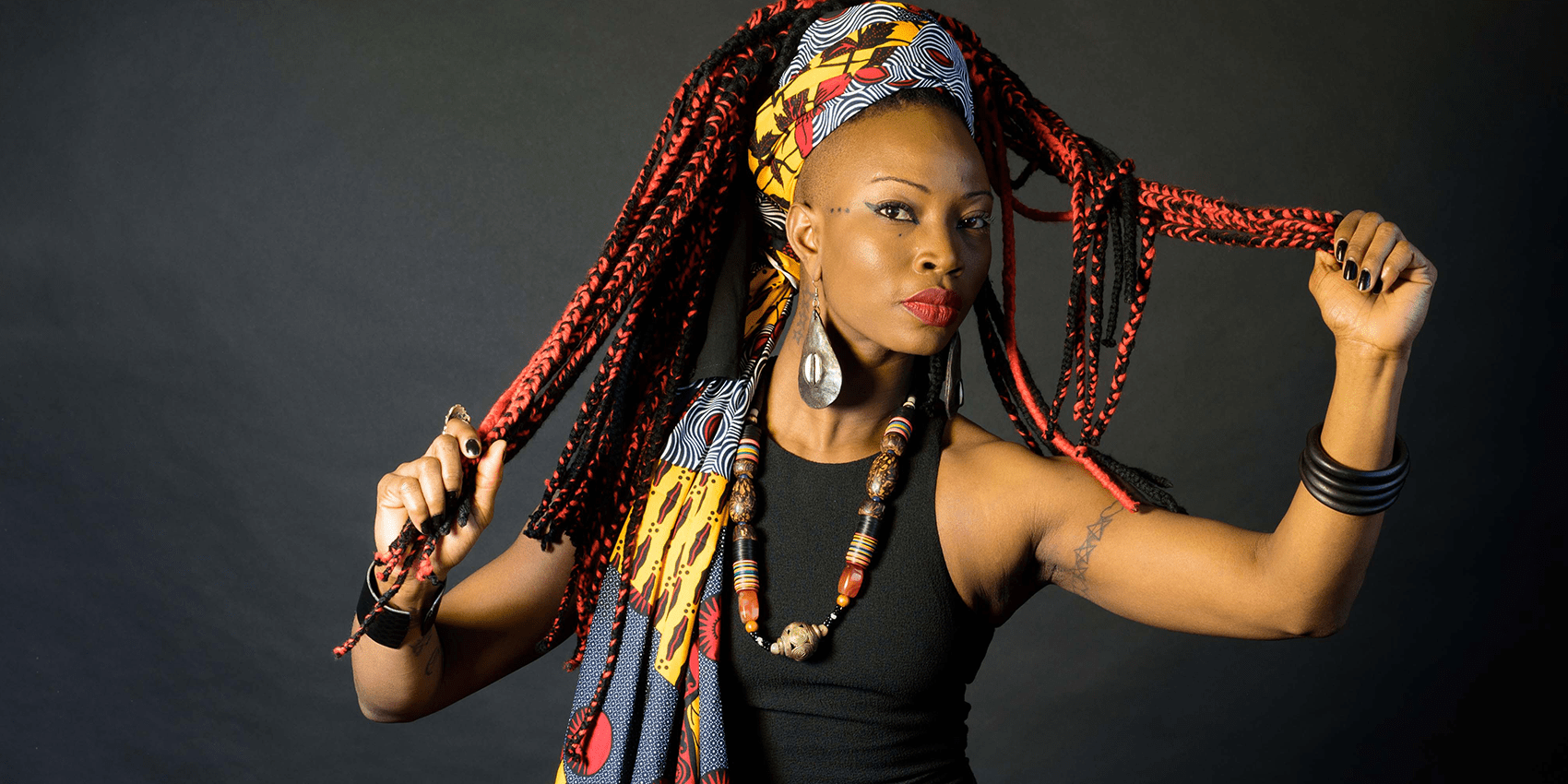 A confident individual showcasing cultural fashion with vibrant dreadlocks and bold accessories.