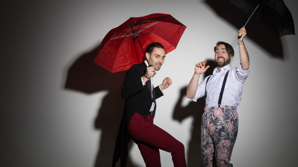 Dynamic duo playfully posing with umbrellas against a shadow-casting backdrop, exuding charm and whimsy.