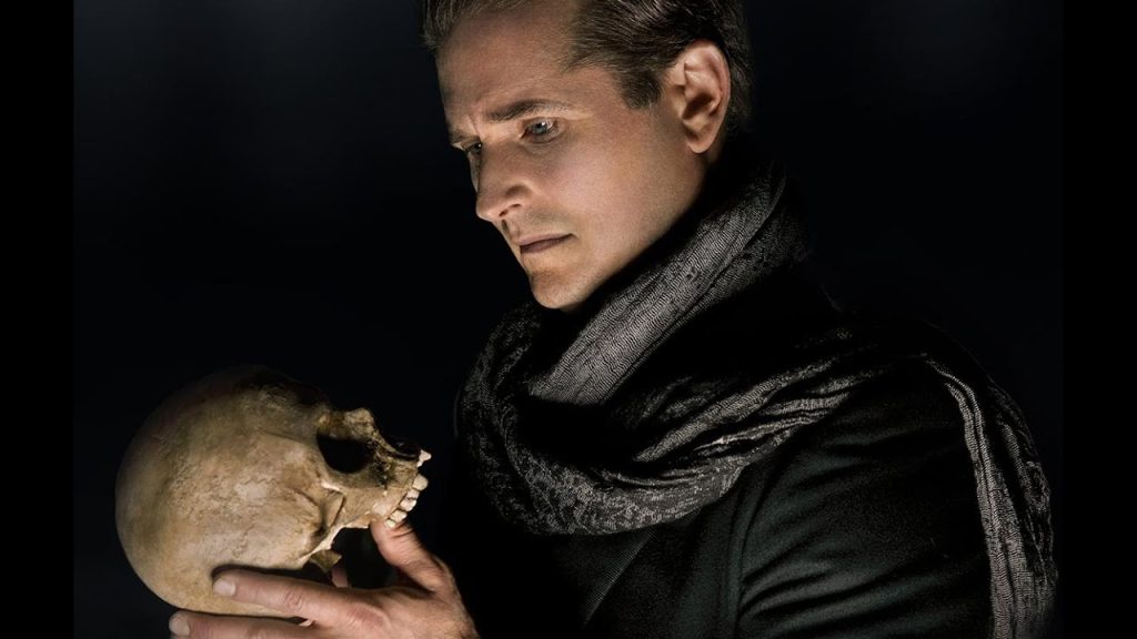 A pensive man gazing intently at a skull he holds in his hand, evoking a scene reminiscent of hamlet's famous soliloquy.
