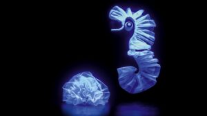 Glowing neon seahorse and jellyfish sculptures floating against a dark background, creating an enchanting underwater scene.
