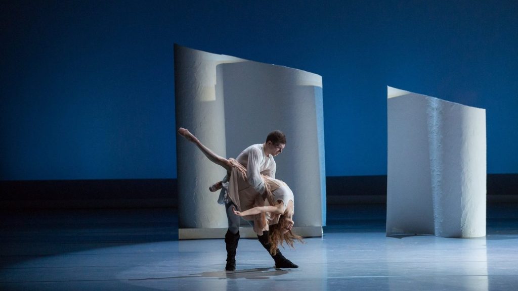 Two ballet dancers in a graceful and emotional pas de deux on a minimalist stage set.