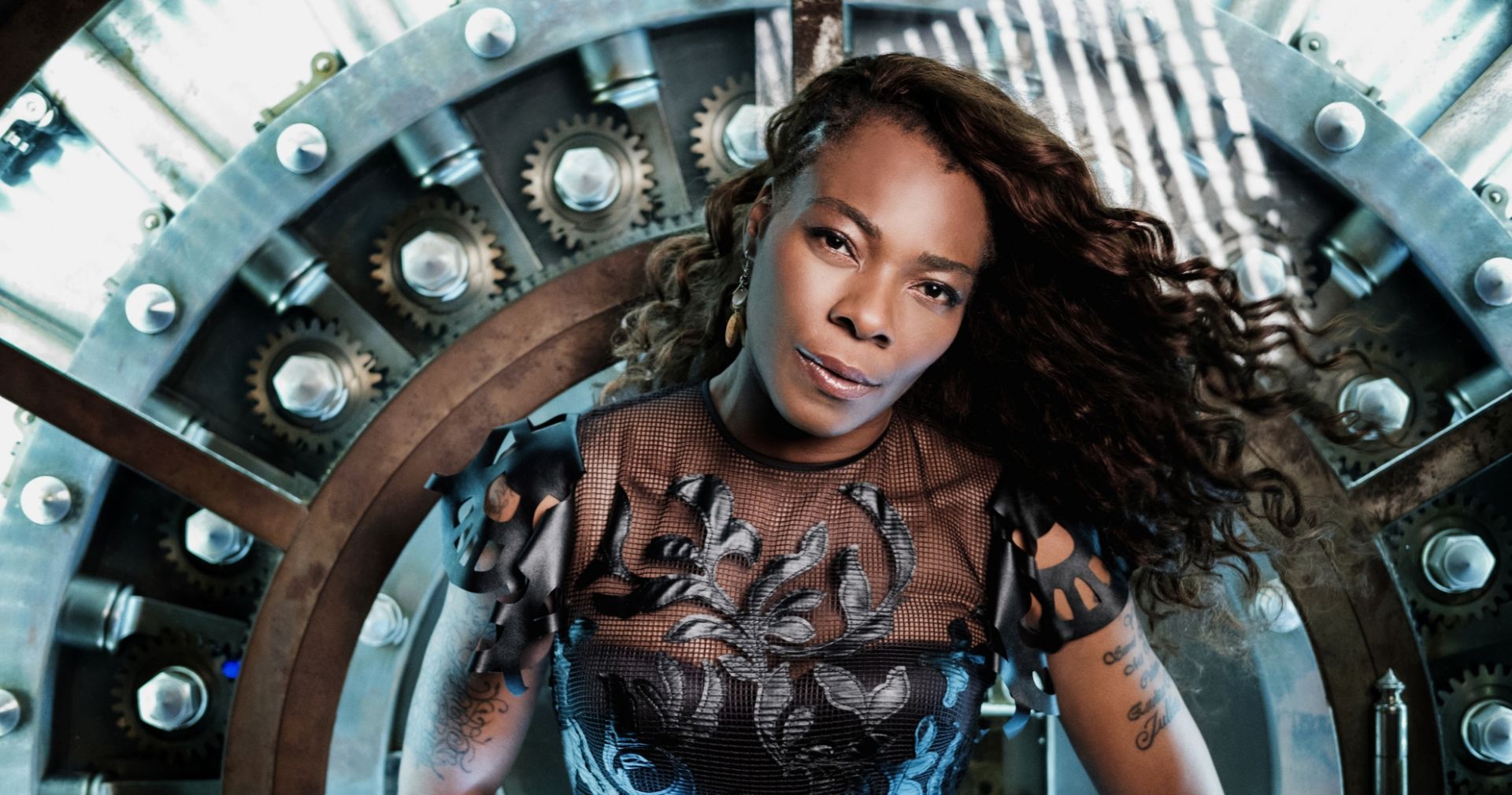 A confident woman in a stylish outfit poses in front of a mechanical, gear-filled backdrop, exuding a futuristic steampunk vibe.