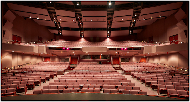 An empty modern theater auditorium with rows of red seats facing a stage, bathed in soft, ambient lighting, awaiting an audience.