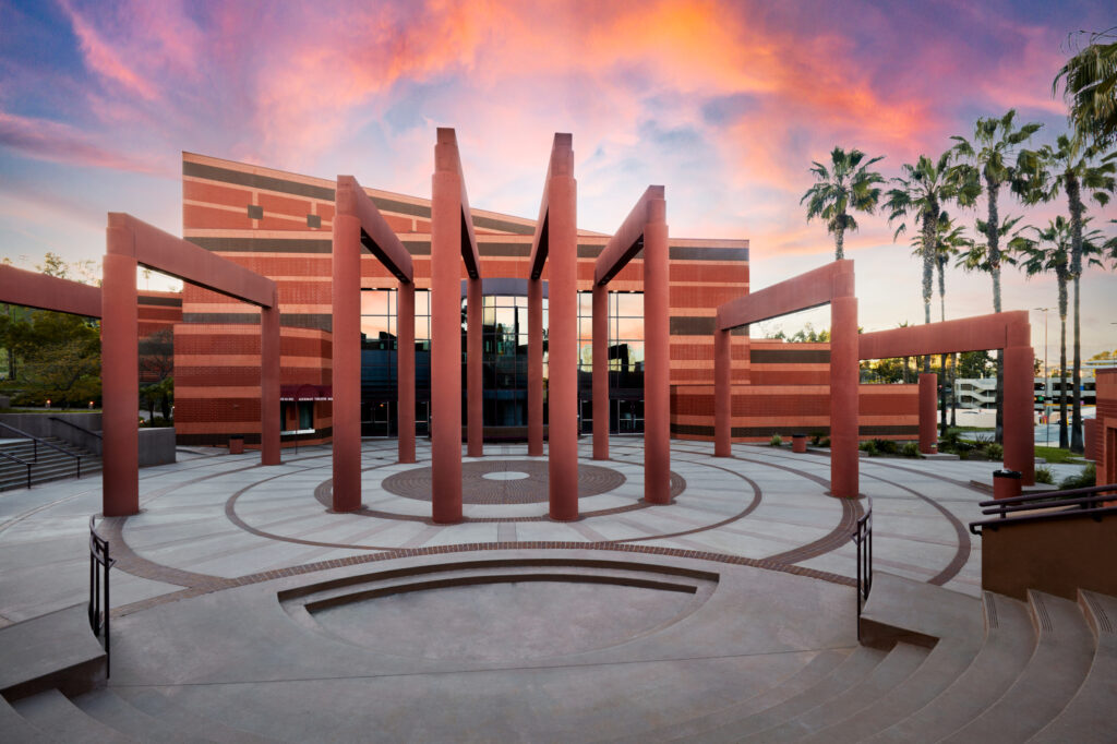 The Street of the Arts featuring terracotta structures against a vibrant sunset sky, complemented by palm trees and a circular courtyard design.