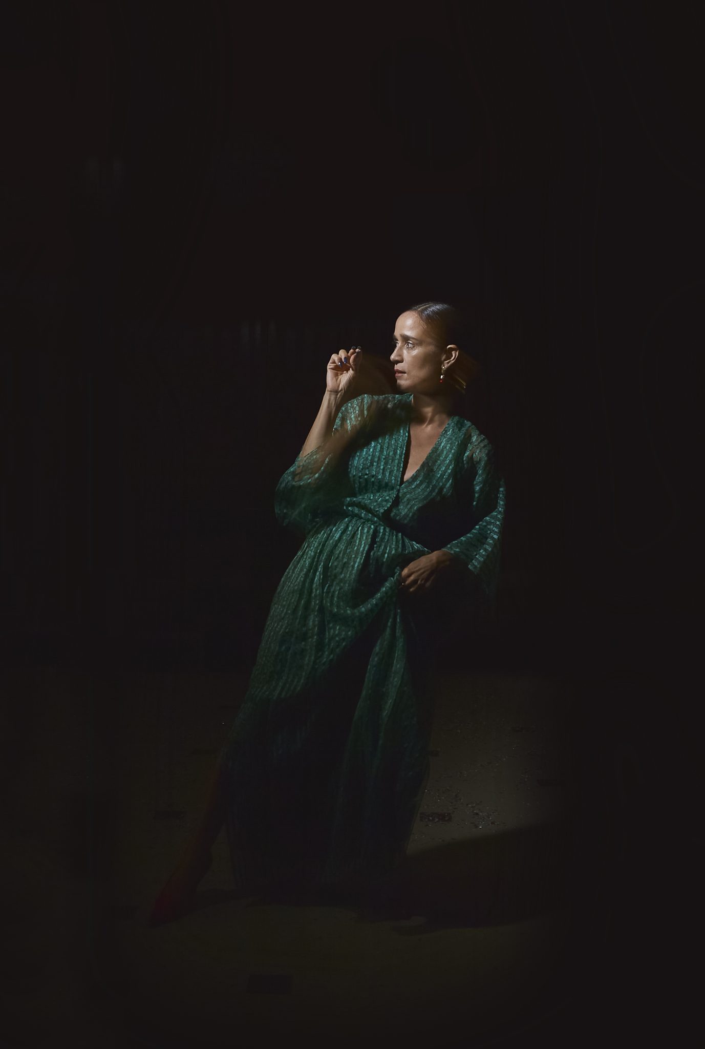 A solitary Julieta Venegas, caught in a contemplative moment, bathed in a sliver of light against the surrounding darkness.