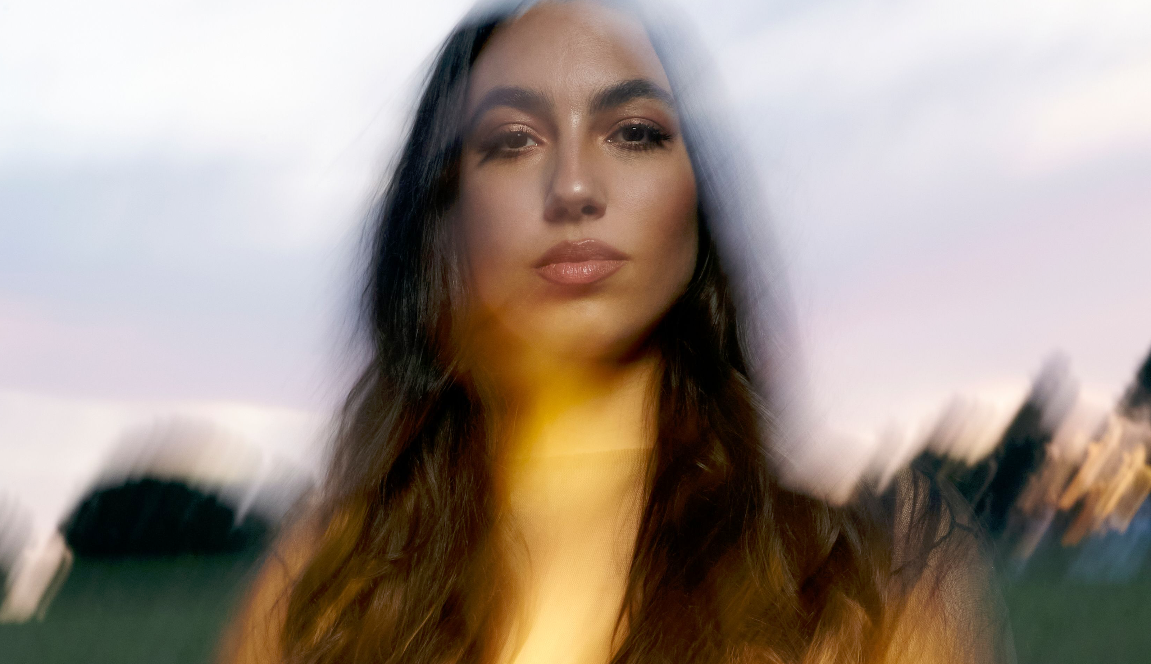 A portrait of María José Llergo with a serene expression, captured with a motion blur effect that gives the image a dreamlike, ethereal quality.