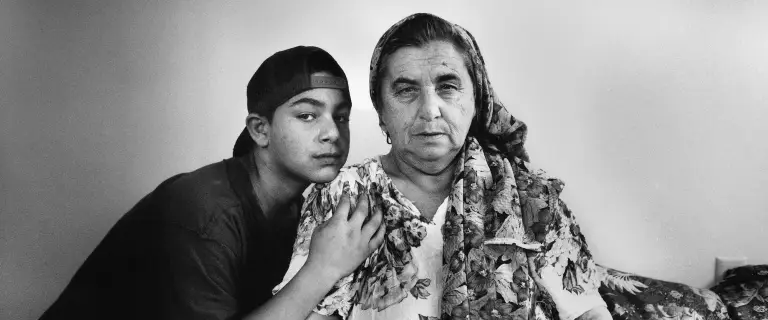 A boy in a backwards cap sits beside an older woman wearing a scarf.