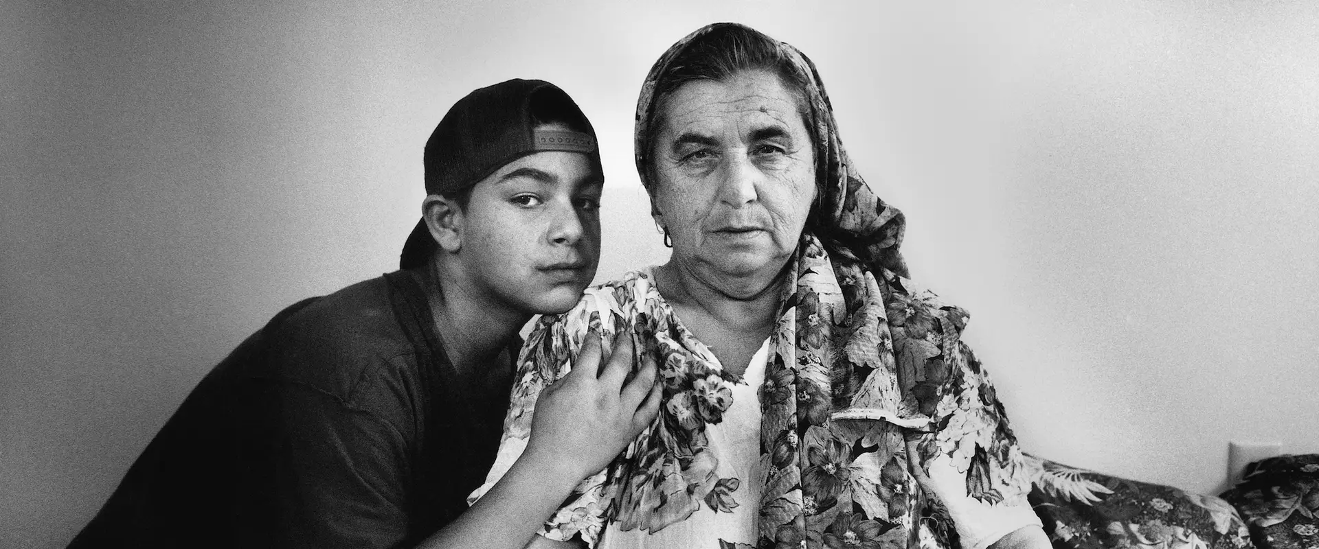 A boy in a backwards cap sits beside an older woman wearing a scarf.