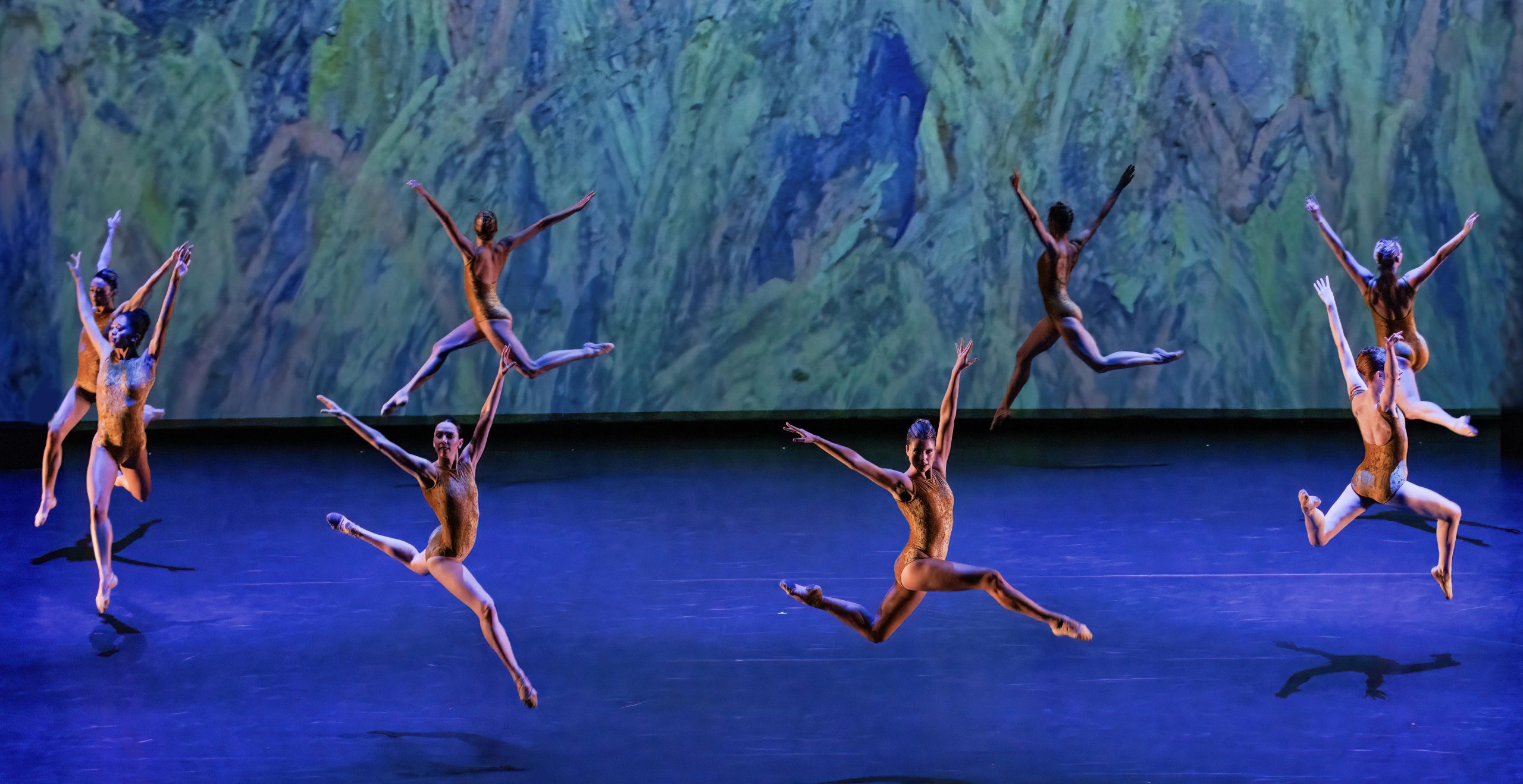 Graceful ballet dancers in perfect unison mid-jump against a painted backdrop, exhibiting the artistry and athleticism of a dance performance.