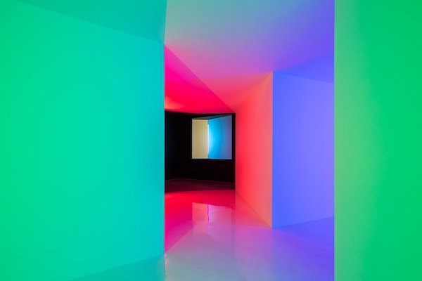 An abstract interior with vibrant neon lights in green, blue, pink, and red hues illuminating sharp geometric walls and a glossy floor, creating a surreal and colorful optical illusion.