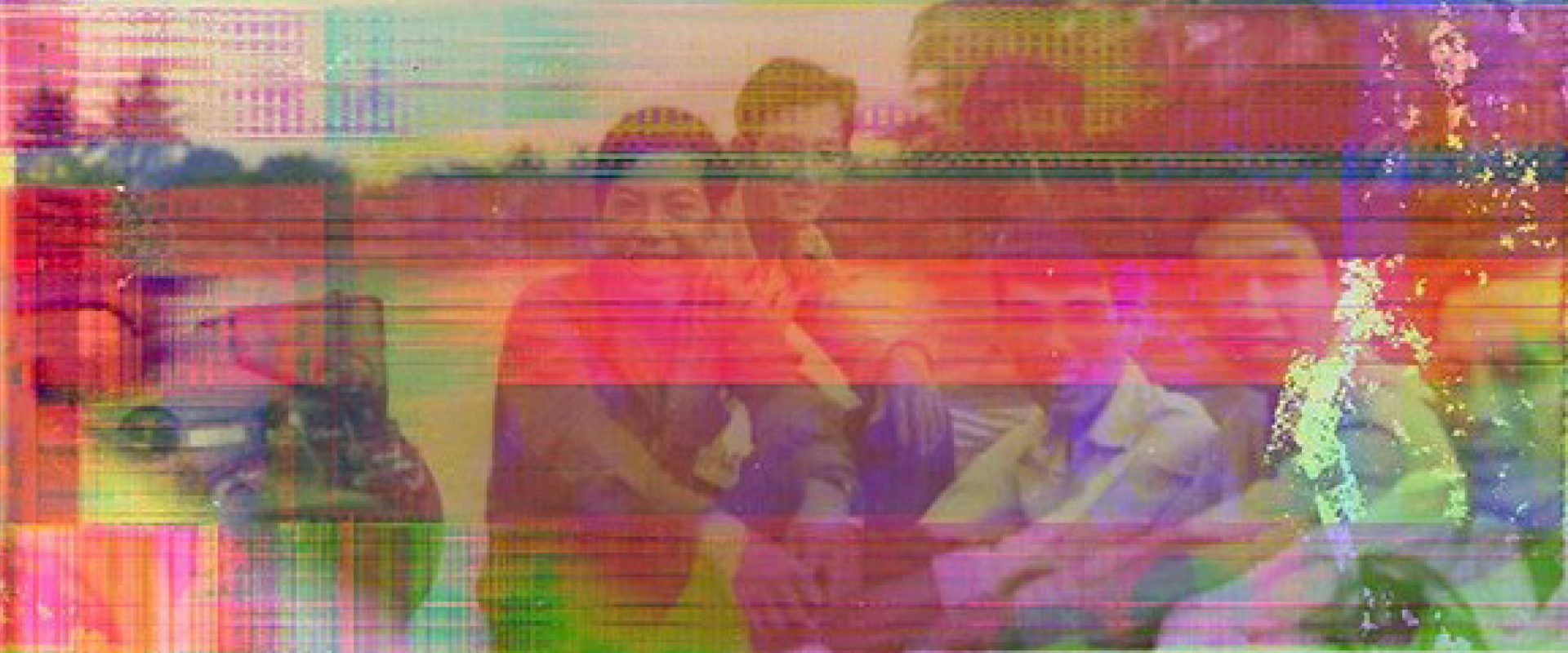 A group of people sit outdoors, smiling at the camera. The photo is distorted with colorful digital glitches and horizontal lines.