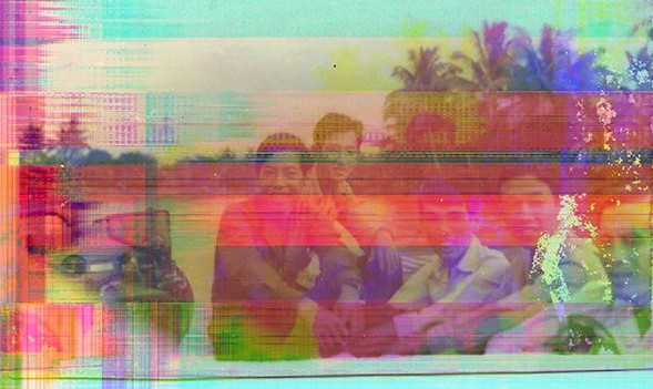 A group of people sitting outdoors with palm trees in the background; the image is heavily distorted by colorful digital glitches and horizontal bands.