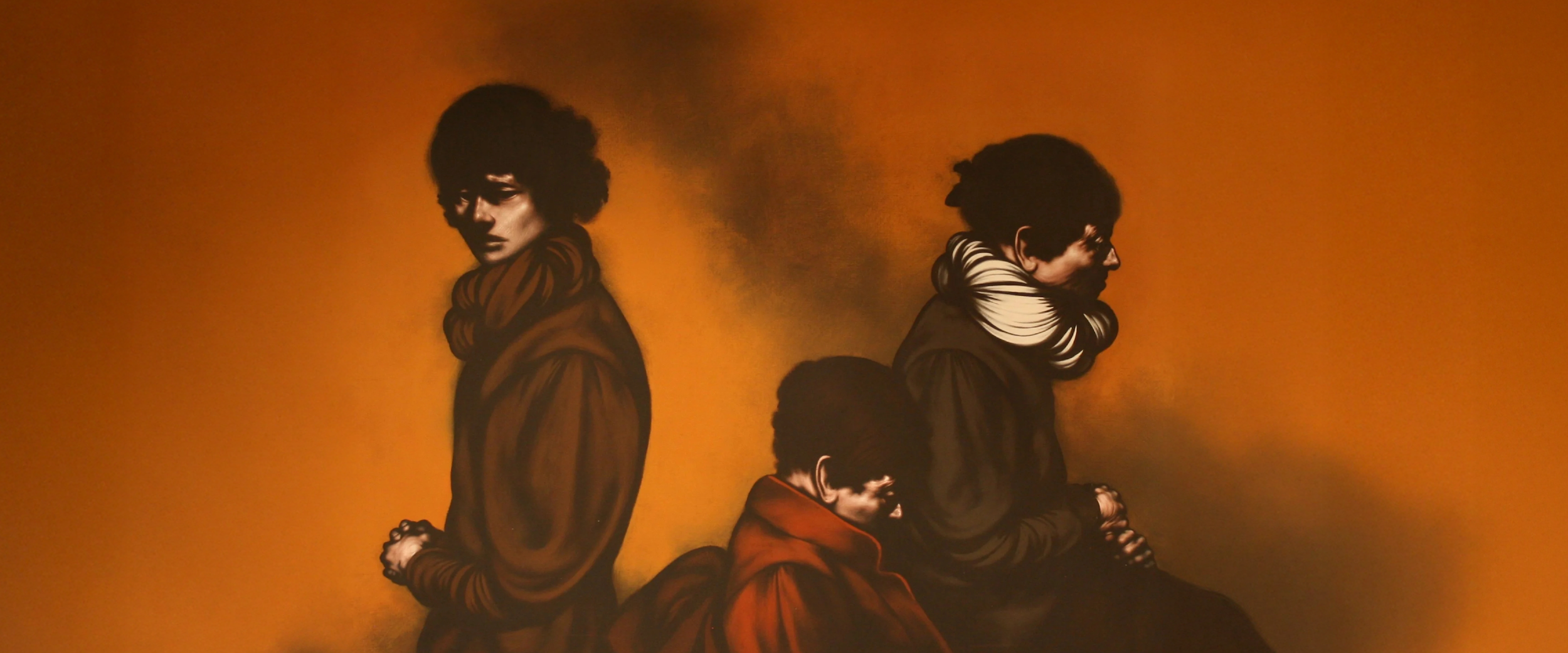 Three figures in dark clothing and dramatic lighting stand and sit against an orange background, each facing a different direction with solemn expressions.