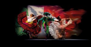 Traditional Mexican dancers in colorful costumes in front of a stylized Mexican fkag backdrop