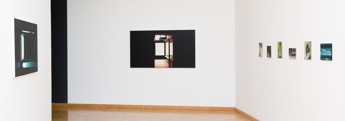 A minimalist art gallery interior with white walls featuring an assortment of framed photographs and paintings displayed at varying heights, with a parquet floor leading up to the artwork.