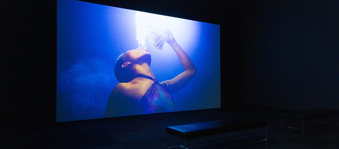 Immersive art experience: a visitor engrossed in a captivating visual projection by The Propeller Group in a dark gallery space.